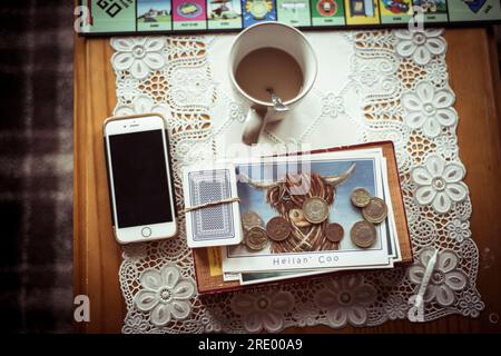 Highland-Kuh-Postkarte mit Münzen, Tee und Telefon auf dem Tisch Stockfoto