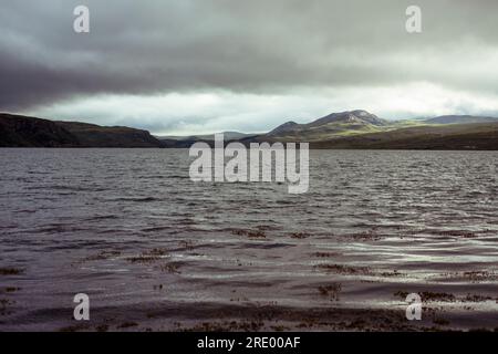 Niedriger Blick über das seidige Wasser des Sees, während die Sonne auf den Bergen untergeht Stockfoto