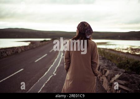 Ein Mädchen mit Bandana geht bei Sonnenuntergang auf einer friedlichen Straße spazieren Stockfoto