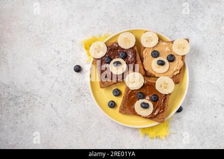 Toast zum Frühstück mit Nussbutter, Banane und Heidelbeere mit niedlichem lustigem Tiergesicht. Kinderessen, Frühstück für Kinder oder Schulessen. Draufsicht Stockfoto