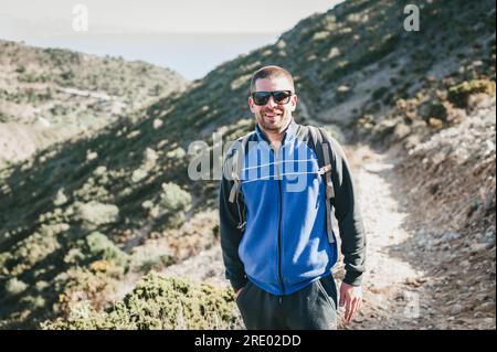 Junger Mann mit Sonnenbrille, der in den Bergen von Malaga, Spanien, vor der Kamera lächelt Stockfoto