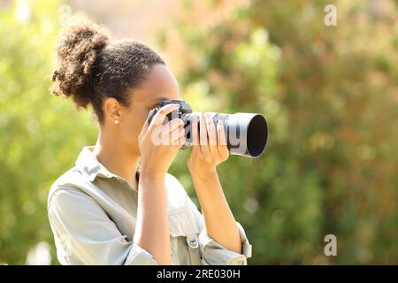 Schwarzer Fotograf, der Fotos im Garten mit einer spiegellosen Kamera macht Stockfoto