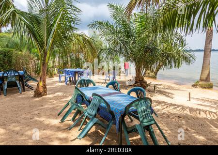 Ein Restaurant mit Tischen und Stühlen wartet am Anderita Beach in Entebbe, Uganda. Palmen am Victoria-See. Stockfoto