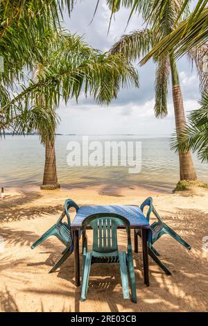 Ein Restauranttisch und Stühle warten auf Anderita Beach in Entebbe, Uganda. Palmen am Victoria-See. Stockfoto