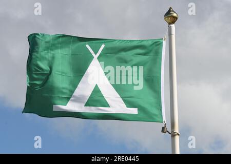 Die Campingflagge winkt im Wind, weißes Zelt auf grünem Hintergrund Stockfoto