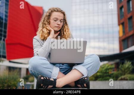 Vollständige Ansicht einer jungen Studentin, die einen Laptop draußen auf dem Campus benutzt. Frauen denken. Stockfoto