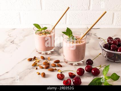 Zwei Gläser frisch zubereiteter Kirsch-Smoothie mit Mandeln und Minze auf einem Marmortisch mit Beeren und Nüssen. Ein köstlicher, gesunder Snack Stockfoto