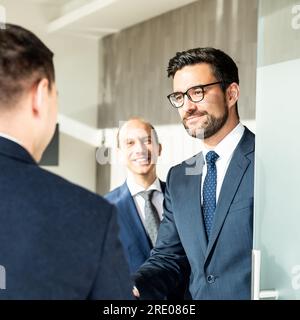Gruppe selbstbewusster Geschäftsleute, die bei einem Geschäftstreffen in einem modernen Büro mit einem Händedruck begrüßt werden. Stockfoto