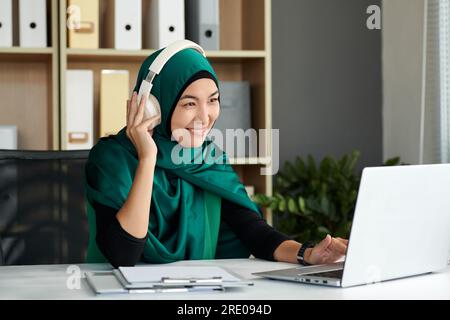 Lächelnde, reife Frau in Hijab, die an einem Laptop im Büro arbeitet Stockfoto