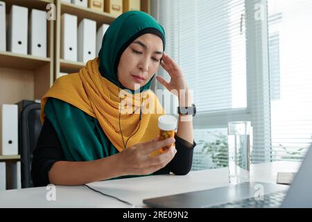 Gestresste, depressive muslimische Geschäftsfrau, die sich Pillen-Container ansieht Stockfoto