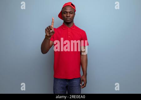 Firmenfarbe. Hübscher afrikaner mit rotem T-Shirt und Mütze auf Hintergrund mit Kopierbereich. Stockfoto
