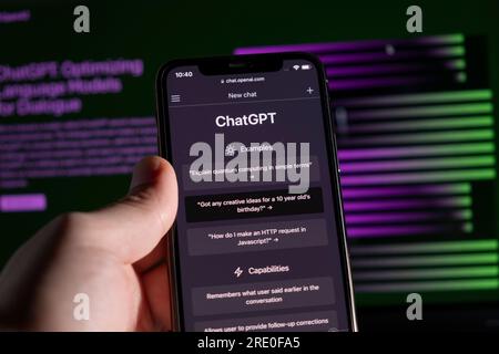 Azoren, Portugal - 21.01.2023: Smartphone-Handheld-ChatGPT-Prompt-Webseite und im Hintergrund verschwommenes ChatGPT-Wortkabel auf einem Laptop-Bildschirm. Stockfoto