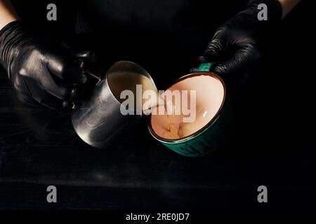 Gekürzt, Barista in Latexhandschuhen bereitet Cappuccino, Espresso, Latte Art, Pitcher mit Milch zu Stockfoto