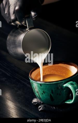 Pitcher, Milch eingießen, Barista in Latexhandschuhen für Cappuccino, aromatischen Espresso, Latte Art Stockfoto