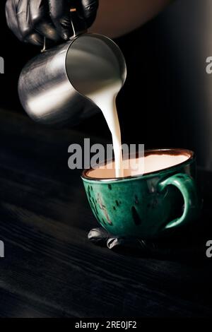 Barista in Latexhandschuhen bereitet Cappuccino, frischen Espresso, Latte Art, Pitcher und Milch zu Stockfoto