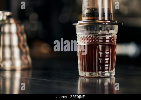 Kristallglas mit aromatischem und frisch gebrühtem Espresso, zubereitet in einer Aero Press-Kaffeemaschine Stockfoto