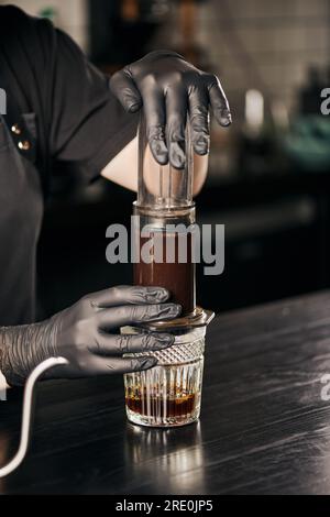 Zugeschnittene Ansicht des Baristas in schwarzen Handschuhen, in der gemahlener Kaffee während der Zubereitung von Espresso in der Aero-Presse gepresst wird Stockfoto