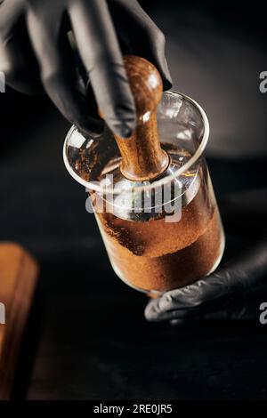 Kurzer Blick auf den Barista in schwarzen Latexhandschuhen, der gemahlenen Kaffee in einer kalten, tropfenden Kaffeemaschine im Café presst Stockfoto