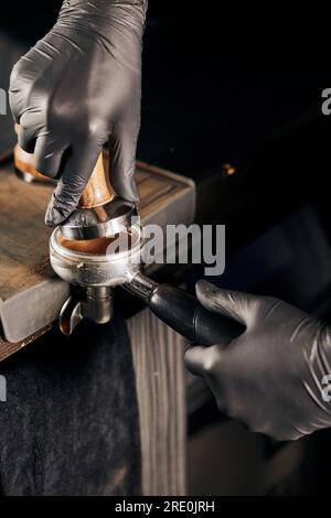 Zugeschnittene Ansicht des Baristas in schwarzen Latexhandschuhen, in der gemahlener Kaffee in den Portafilter gedrückt wird Stockfoto