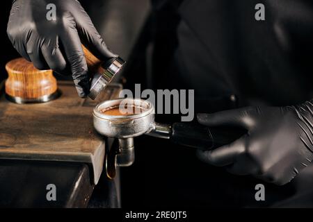 Kurzer Blick auf den Barista in schwarzen Latexhandschuhen, der gemahlenen Kaffee in Portafilter, Café presst Stockfoto