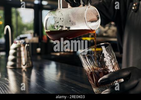 Teilweise Blick auf den Barista, der aromatischen Espresso aus der Kaffeekanne in Kristallglas im Café gießt Stockfoto