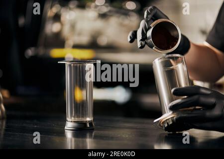 Teilansicht des Baristas, der Espresso zum Übergießen bereitstellt und gemahlenen Kaffee in der Aero Press ausgießt Stockfoto