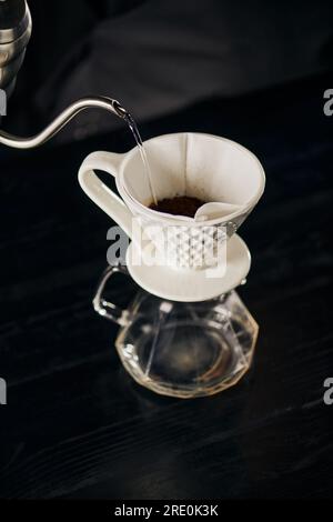 Kochendes Wasser gießt auf gemahlenen Kaffee in einem Keramiktrockner auf einer Glaskanne, V-60-Espresso Stockfoto