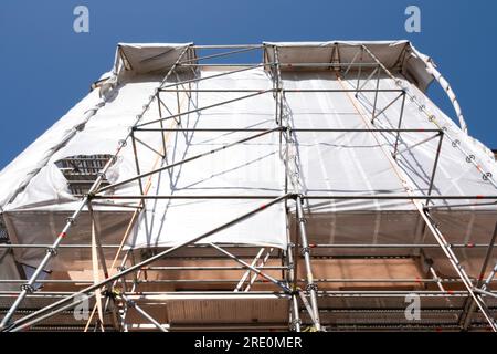 Gerüste mit Schutzlappen um ein Gebäude, um zu verhindern, dass Baumaterial während der Renovierung auf die Straße und auf Menschen fällt Stockfoto