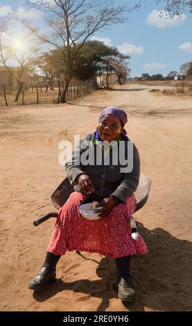 Dorfleben, alte afrikanerin, die in einer Schubkarre saß, Eintopf aß und aus dem Herzen lachte Stockfoto