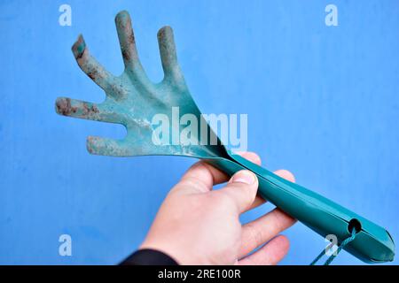 Kleiner grüner Gartenrechen in der Hand auf blauem Hintergrund Stockfoto