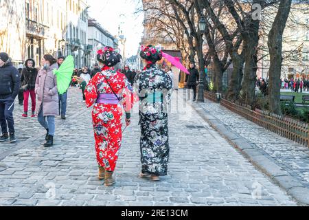 Lemberg, Ukraine - 07. Januar 2022: Zwei junge Frauen in traditionellem japanischem Kimono mit Regenschirmen, die durch die Stadt laufen, Rückblick Stockfoto