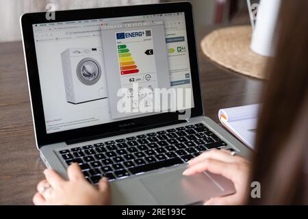 Eine Frau konsultiert das Energieetikett einer Waschmaschine bei einem Online-Gerätehändler. Energieetikettierung von Geräten auf einer Skala von A bis G accordi Stockfoto
