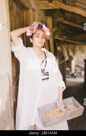 Wunderschöne indianerin in einem weißen Kleid und einem Kranz auf dem Kopf hält einen Korb mit Mais. Die Farm oder das Land Stockfoto