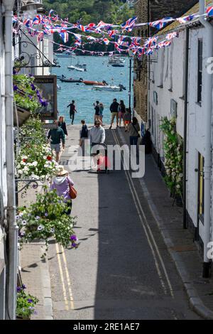 Blick auf die Fore Street, Salcombe, mit Blick auf das ruhige Wasser der Flussmündung, Union Jack Fliegerei mit Menschen, die in der Sonne wandern. Stockfoto