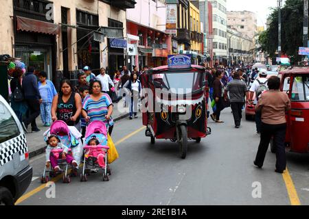 Frauen, die Mädchen in Kinderwagen und motorisiertem Dreiradtaxi (Mototaxi) in der kommerziellen Marktgegend von Zentral-Lima, Peru, schieben Stockfoto