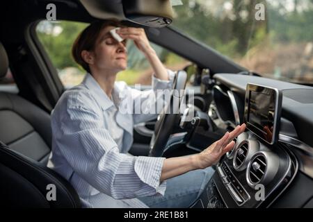 Frau fährt Auto mit kaputter Klimaanlage bei heißem Wetter wischt Schweiß auf Gesicht. Stockfoto
