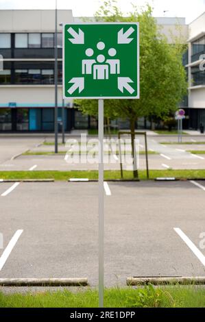 Schild für Sammelstelle auf einem Firmenparkplatz, grünes Schild mit weißen Pfeilen, Schild zur Kennzeichnung ausgewiesener sicherer Orte, an denen sich Personen treffen können oder müssen Stockfoto