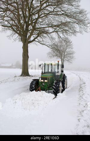 Bauer, der Schnee von einer Landstraße räumt. Bauer, der Zufahrtsstraßen zu einem Dorf räumt Stockfoto