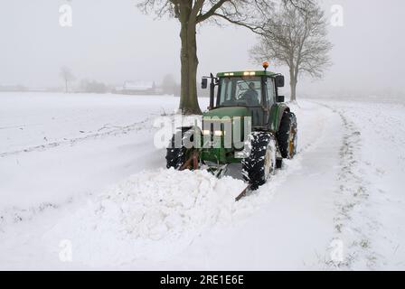 Bauer, der Schnee von einer Landstraße räumt. Bauer, der Zufahrtsstraßen zu einem Dorf räumt Stockfoto