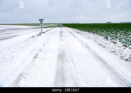 Verschneite und vereiste Landstraße, Schneeverwehungen am Straßenrand und hohe Verkehrsbedingungen Stockfoto
