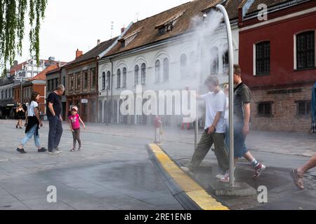 Jungs gehen durch einen Metallbogen eines Wasserreglers, um sich vom Beschlagen abkühlen zu lassen, auf einem Platz in Kaunas. Gefahr der Legionellenkontamination Stockfoto