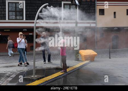 Das Mädchen wird von einer Wassersprühanlage auf einem Platz in Kaunas gekühlt. Ihre Eltern fotografieren es. Gefahr der Legionellenkontamination Stockfoto