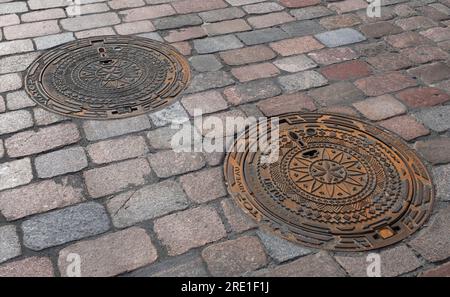 Zwei dekorierte Mannlochdecken in einer Straße in der litauischen Stadt Kaunas Stockfoto