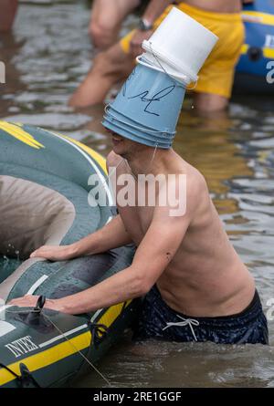 Ulm, Deutschland. 24. Juli 2023. Ein junger Mann trägt Wassereimer auf dem Kopf auf der Donau während der Nabada. Die Nabada (Schwimmen nach unten) ist eine Art Karnevalsprozession und bildet den Höhepunkt von Schwörmontag. Seit etwa 600 Jahren hat der Oberhaupt Ulms am vorletzten Montag im Juli einen Eid auf die Stadtverfassung geschworen. Danach findet in der Stadt eine große Feier statt. Kredit: Stefan Puchner/dpa/Alamy Live News Stockfoto