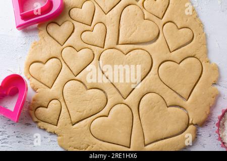 Herzförmige Kekse mit Keksschneider auf einer hellblauen Tischplatte schneiden, Draufsicht. Bühne der Zubereitung von köstlichem hausgemachtem Gebäck Stockfoto