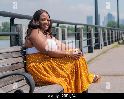 Eine afroamerikanische Frau auf ihrem Telefon, draußen auf einer Bank Stockfoto