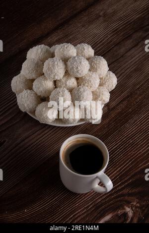Fotografieren Sie eine Tasse Kaffee und einen Teller Süßigkeiten in Kokosflocken auf einem Holztisch Stockfoto