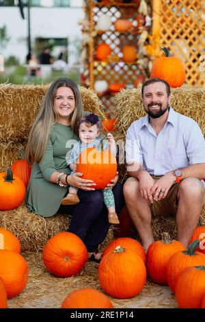 Happy Halloween and Thanksgiving - eine lächelnde Familie und eine kleine Tochter im Hintergrund orangefarbener Kürbisse im Urlaub Stockfoto