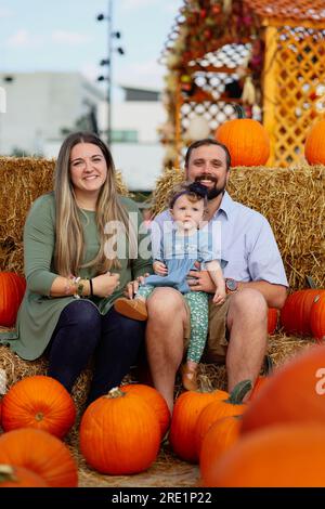 Happy Halloween and Thanksgiving - eine lächelnde Familie und eine kleine Tochter im Hintergrund orangefarbener Kürbisse im Urlaub Stockfoto