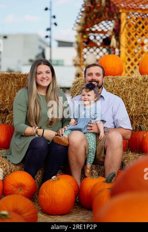 Happy Halloween and Thanksgiving - eine lächelnde Familie und eine kleine Tochter im Hintergrund orangefarbener Kürbisse im Urlaub Stockfoto